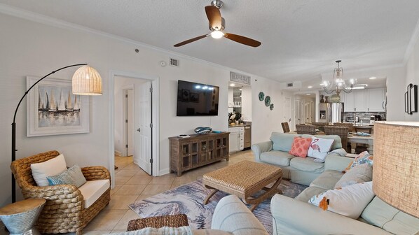 A spacious living room with a large TV, wicker furniture, and a ceiling fan. - The Enclave #1006 by Southern Vacation Rentals (Orange Beach)
