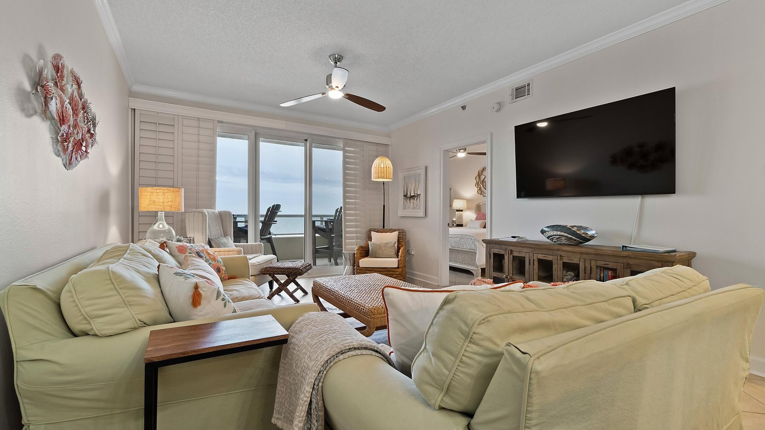 A living room with a sofa, a coffee table, a TV, and a view of the ocean through large windows.