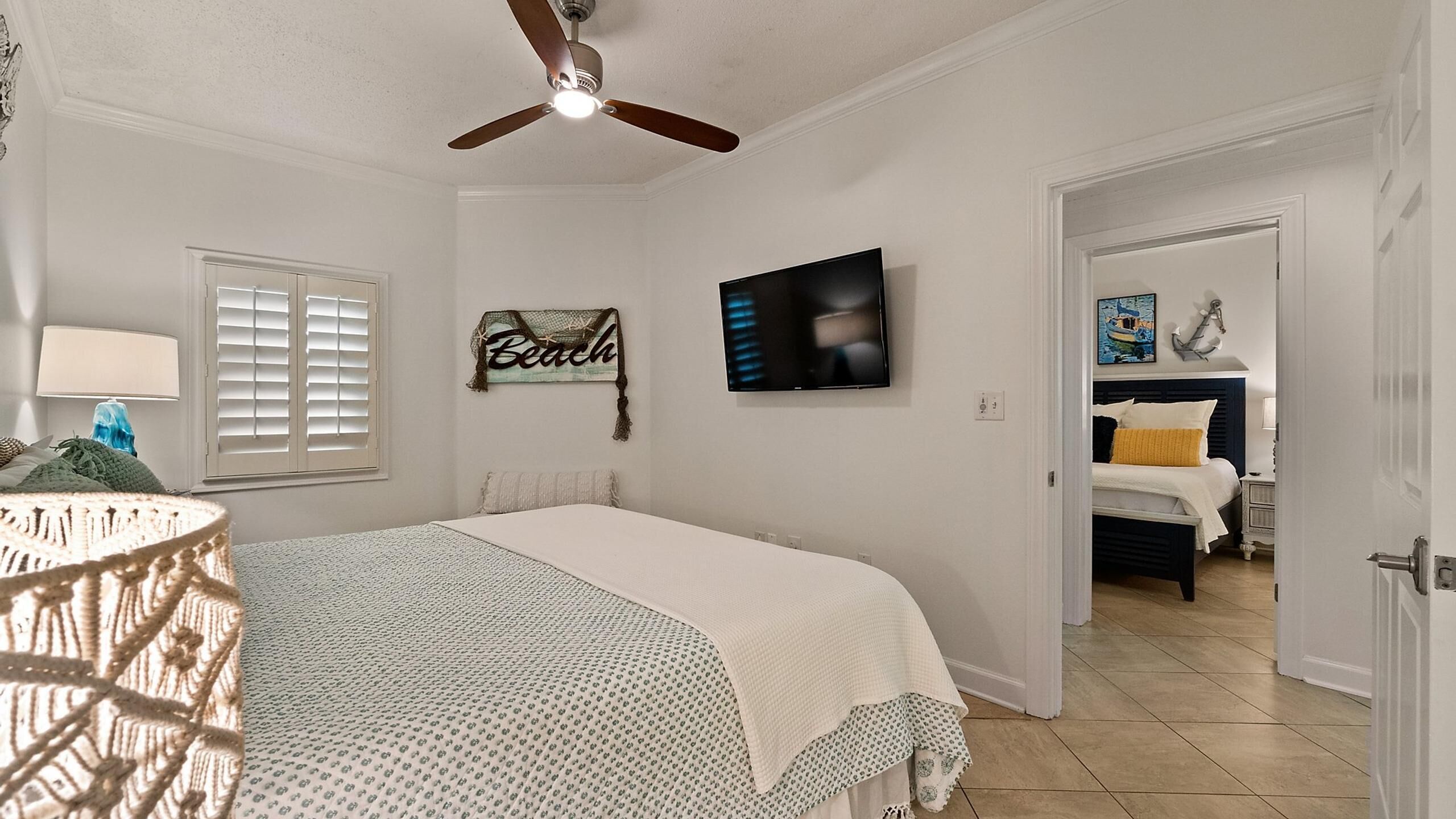 Une chambre à coucher comprenant un lit, un ventilateur de plafond, un téléviseur et une porte donnant sur une autre pièce.