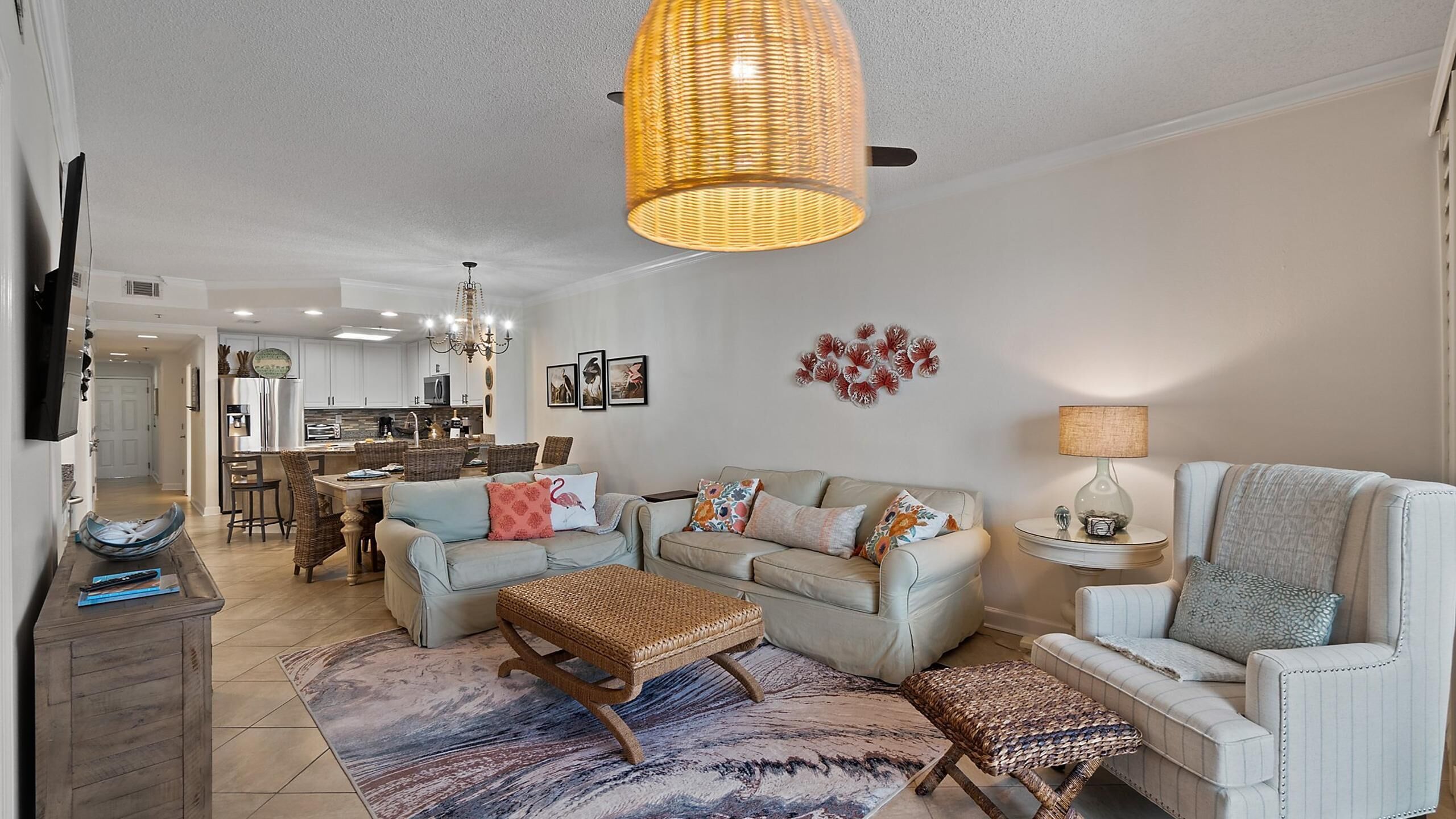 A spacious living room with a large chandelier, a dining area, and a kitchen in the background.