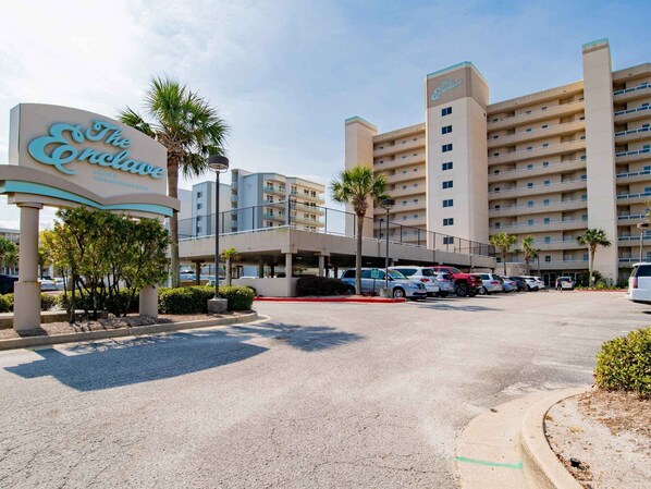 A hotel with a sign reading "The Enclave," featuring a multi-story building with a parking lot in front. - The Enclave #1006 by Southern Vacation Rentals (Orange Beach)