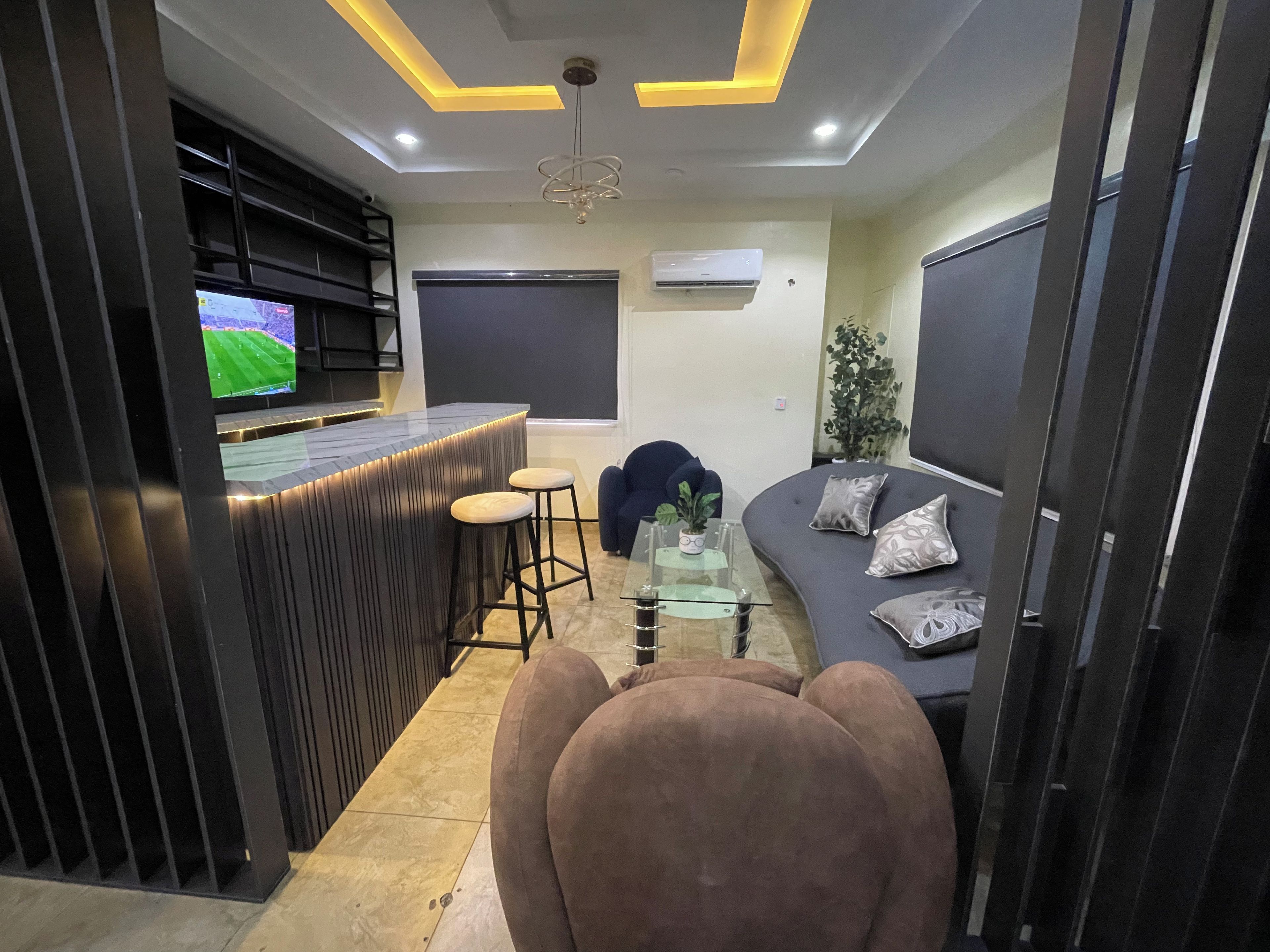 Un espacio moderno de sala con barra, asientos y un televisor mostrando un evento deportivo.