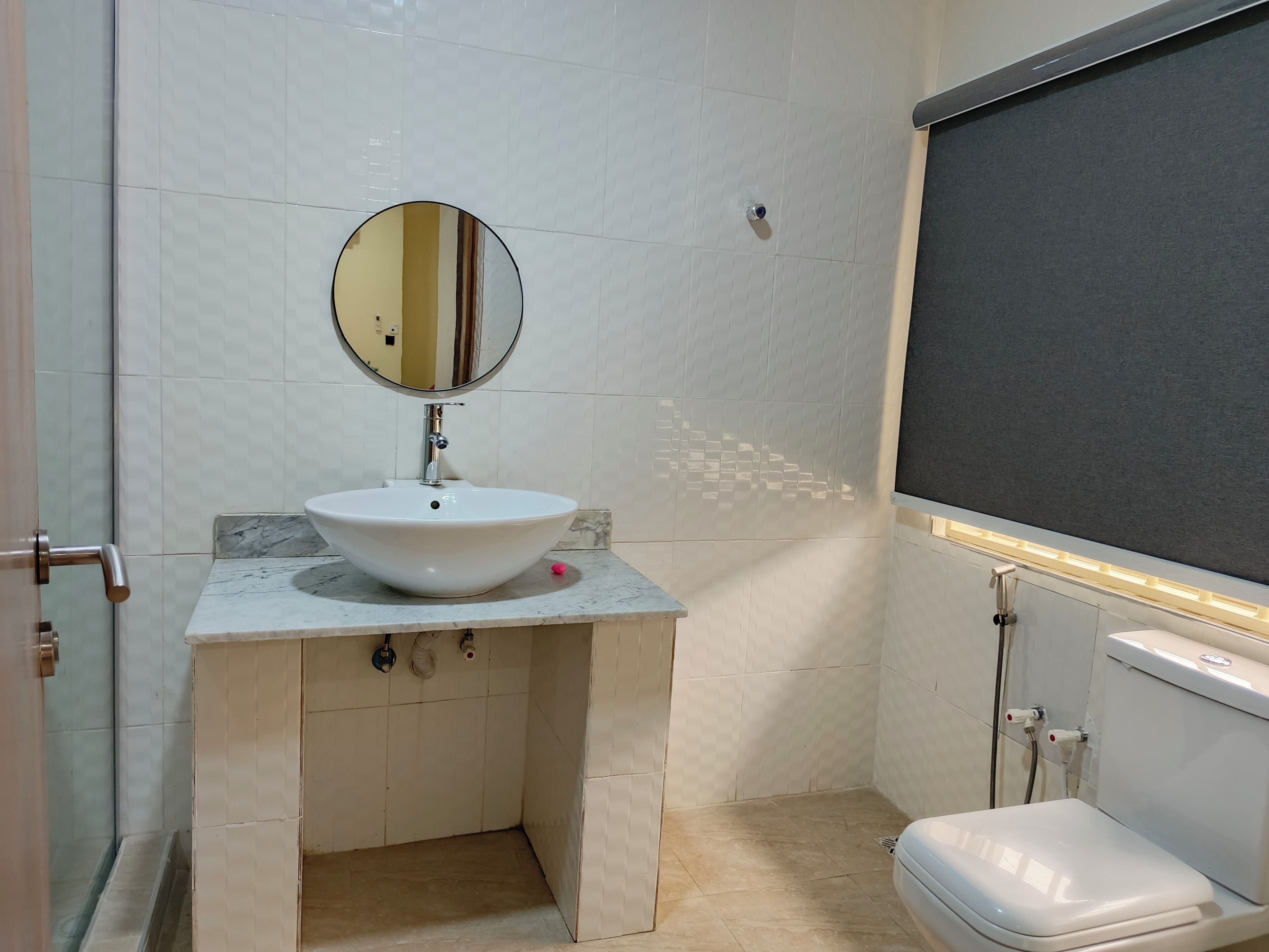 A bathroom with a white sink, a round mirror, a toilet, and a shower area.