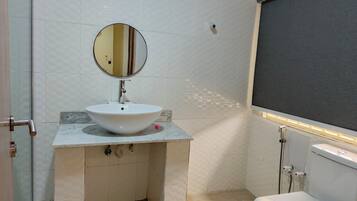 Un baño con un lavabo blanco, un espejo redondo, un inodoro y una zona de ducha.