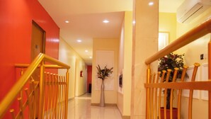 Un couloir d’hôtel avec un mur rouge, un escalier en bois recouvert d’une moquette rouge et une plante en pot.
