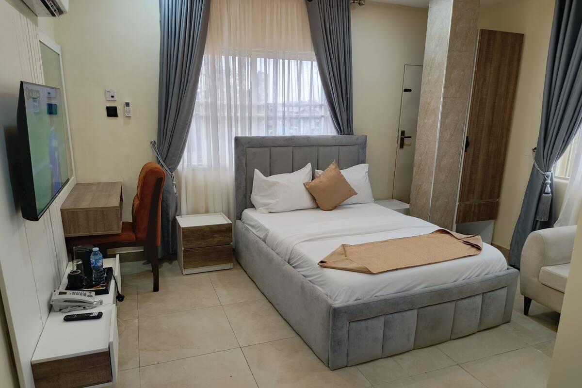 Une chambre d’hôtel avec un lit, un bureau avec un téléphone, une chaise et un téléviseur.