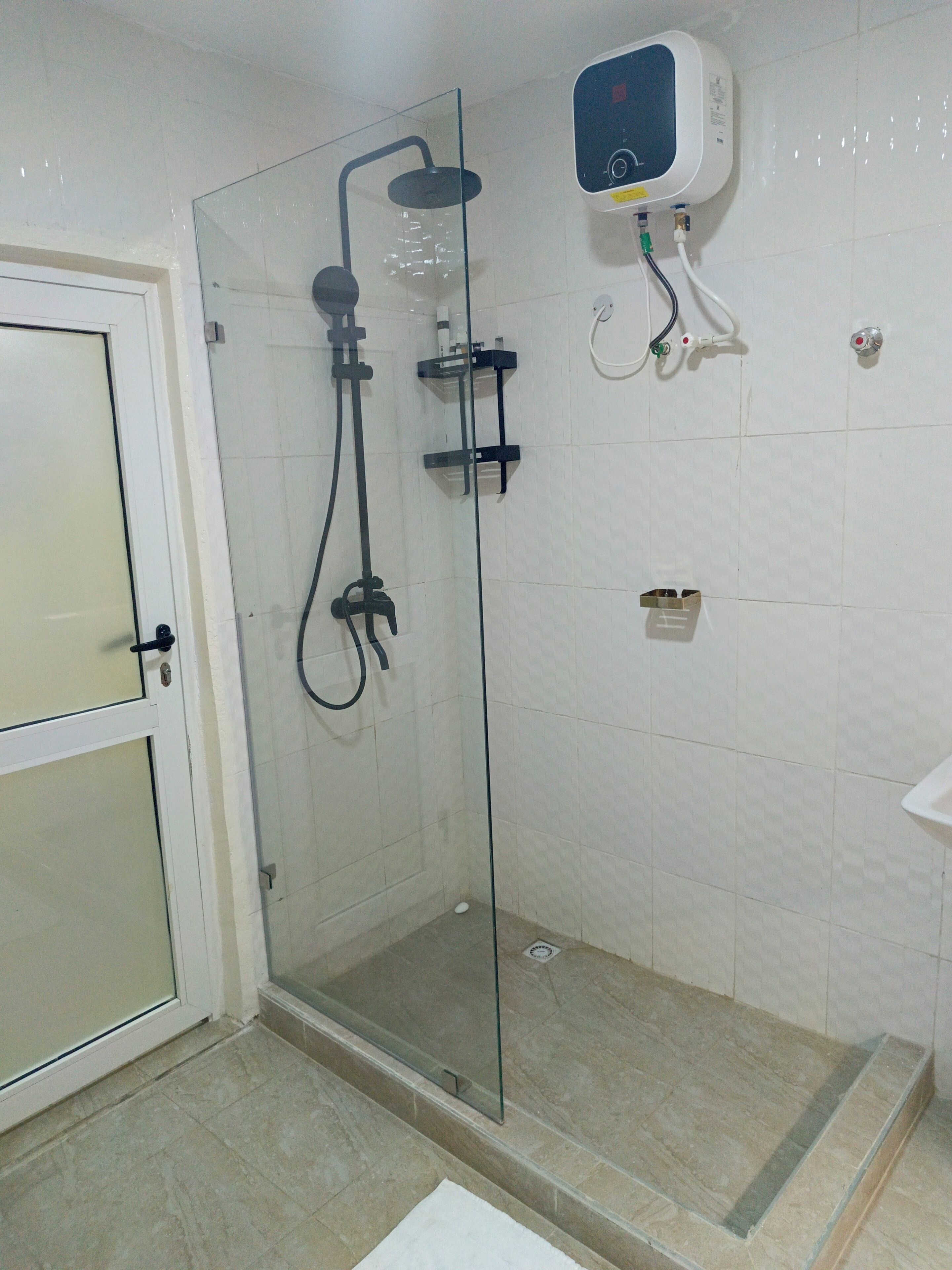 A glass-enclosed shower with a handheld showerhead, a wall-mounted control panel, and a tiled floor.