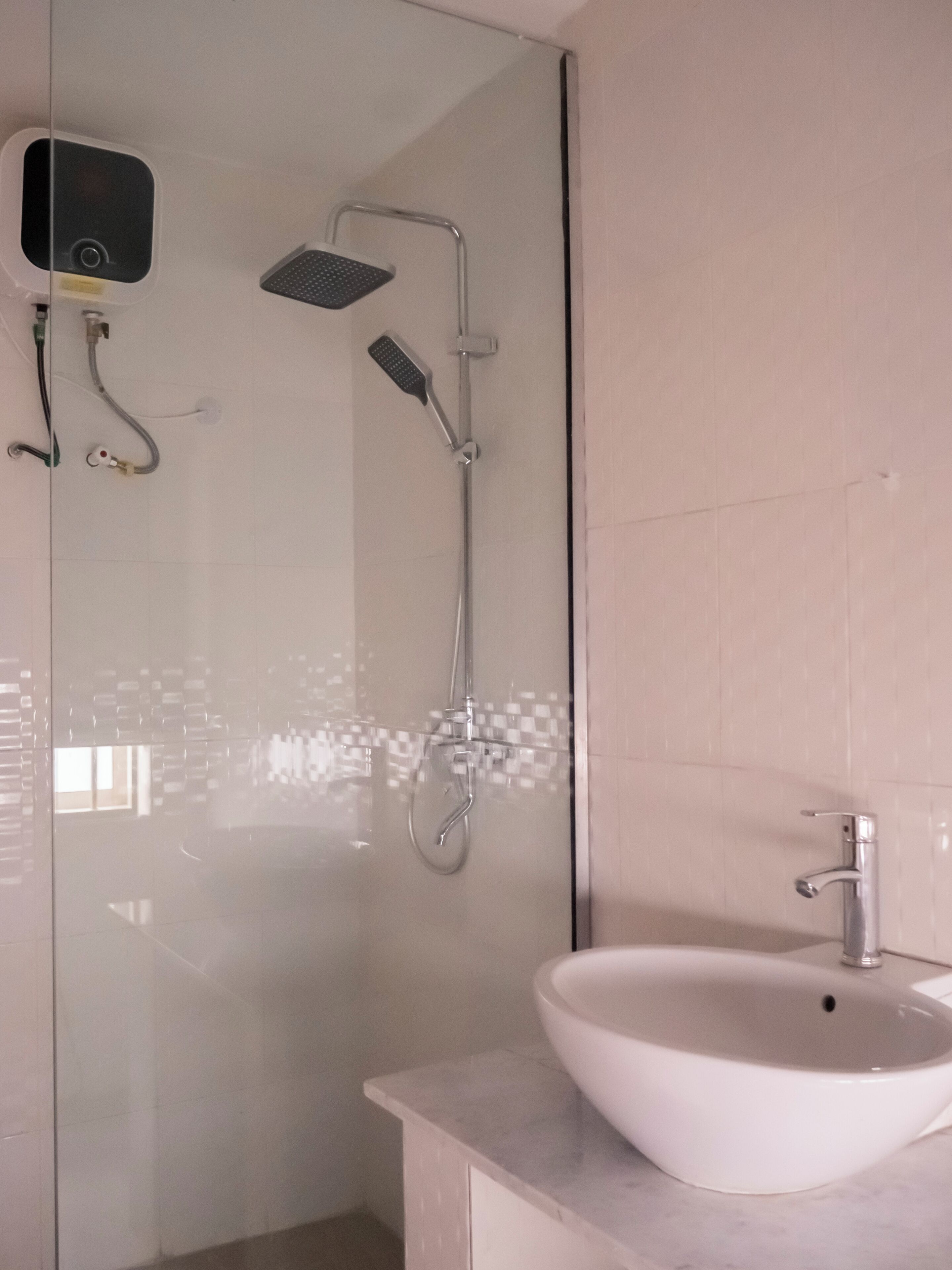 A modern bathroom with a glass shower enclosure, a handheld showerhead, a wall-mounted faucet, and a white sink.