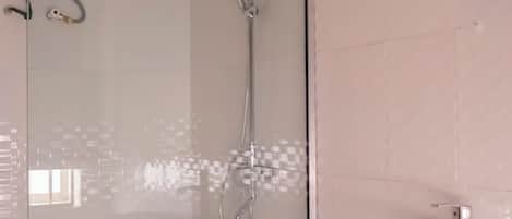 A modern bathroom with a glass shower enclosure, a handheld showerhead, a wall-mounted faucet, and a white sink.