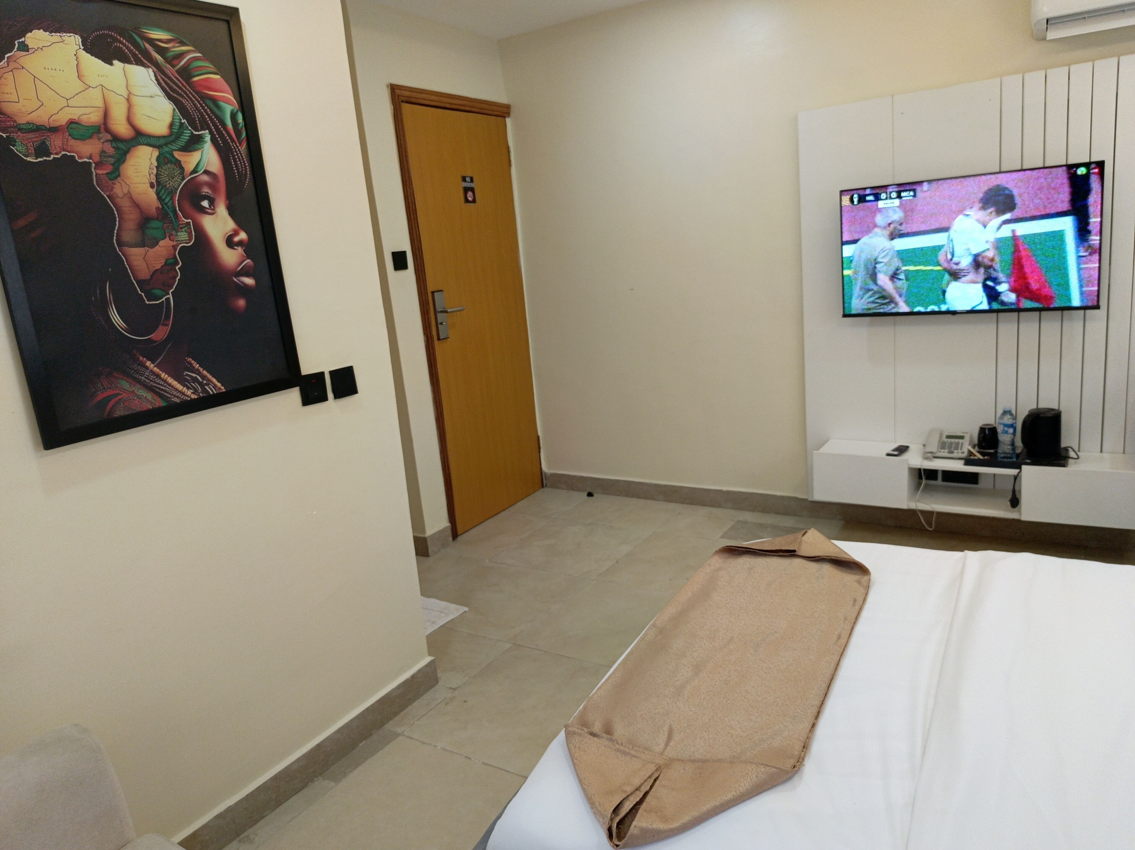 A hotel room with a bed, a television, a painting, and a door.
