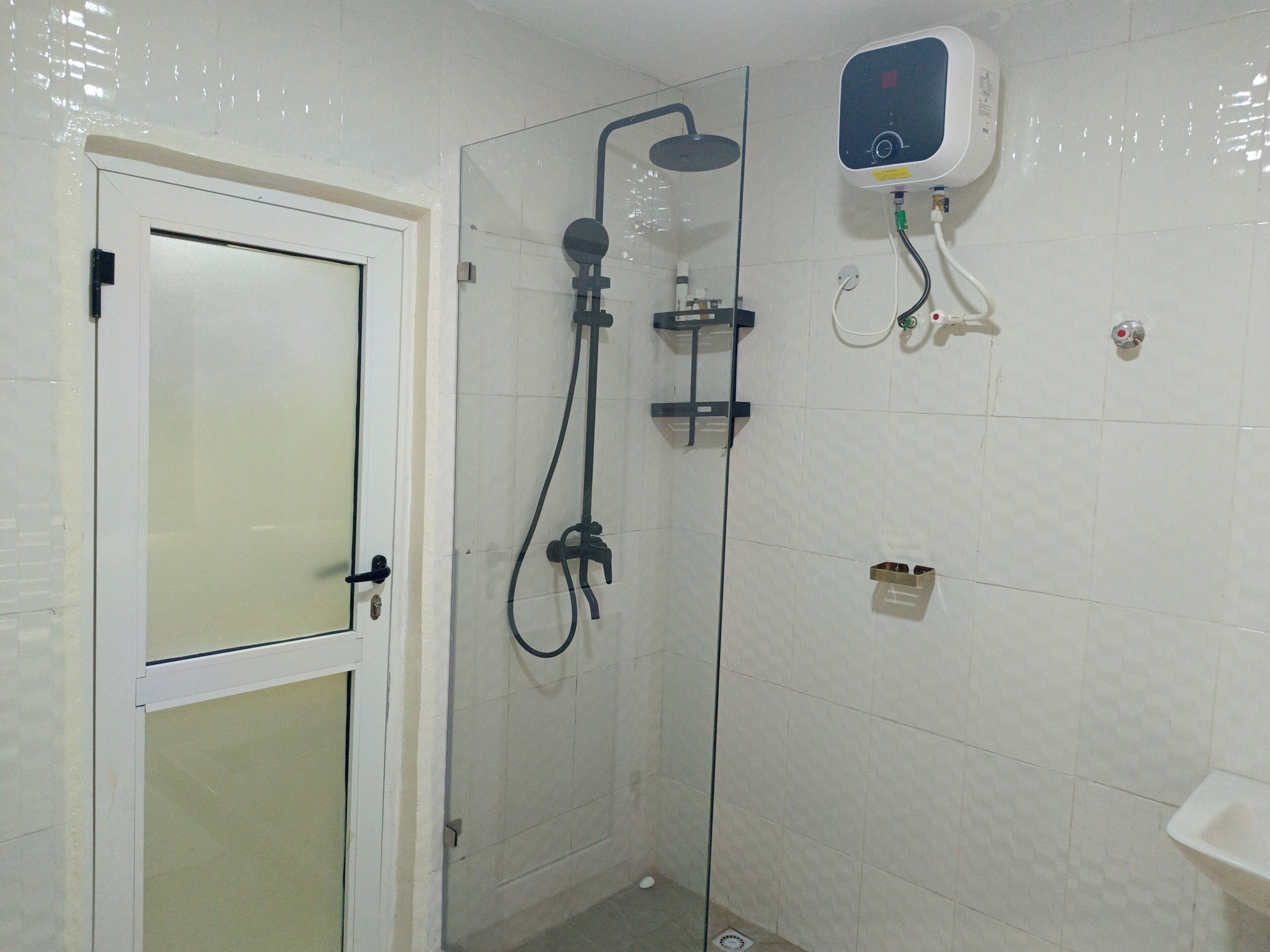 Un baño con puerta de cristal, ducha con cabezal de ducha manual, panel de control en la pared y un lavabo pequeño.