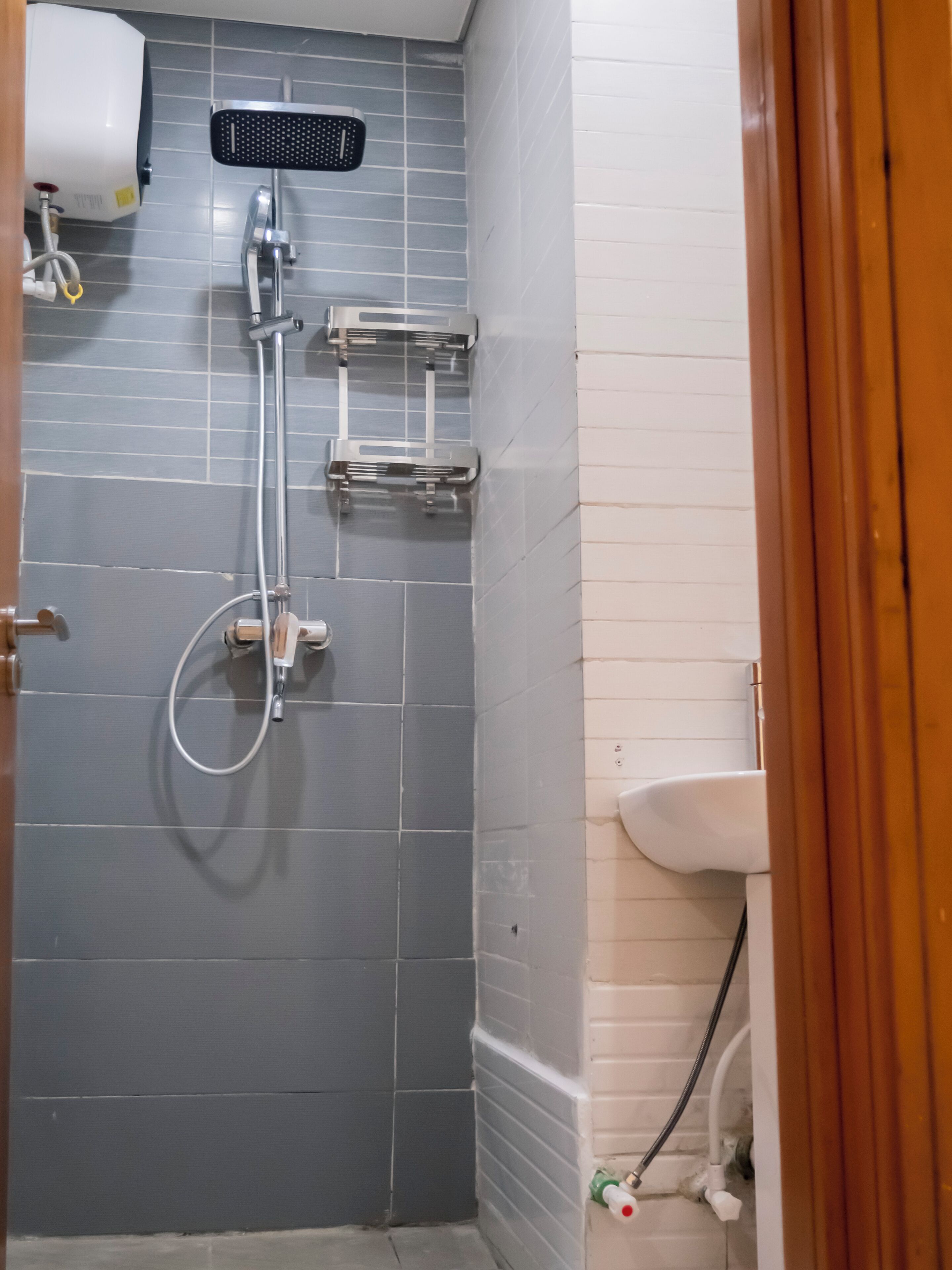 Un baño con paredes de azulejos grises, una ducha con cabezal de ducha manual, un lavamanos blanco y un perchero para toallas.