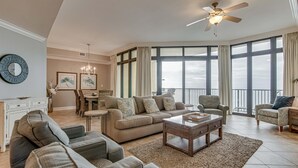 A spacious living room with a large sofa, a coffee table, and a dining area with chairs and a chandelier.