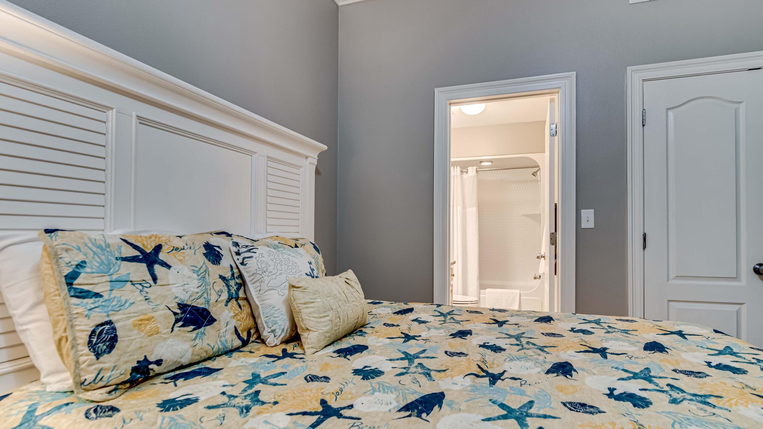Une chambre à coucher avec un lit agrémenté d’une couvre-lit sur le thème de la marine, d’une tête de lit blanche et d’une porte donnant accès à une salle de bain.
