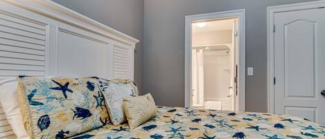 Une chambre à coucher avec un lit agrémenté d’une couvre-lit sur le thème de la marine, d’une tête de lit blanche et d’une porte donnant accès à une salle de bain.