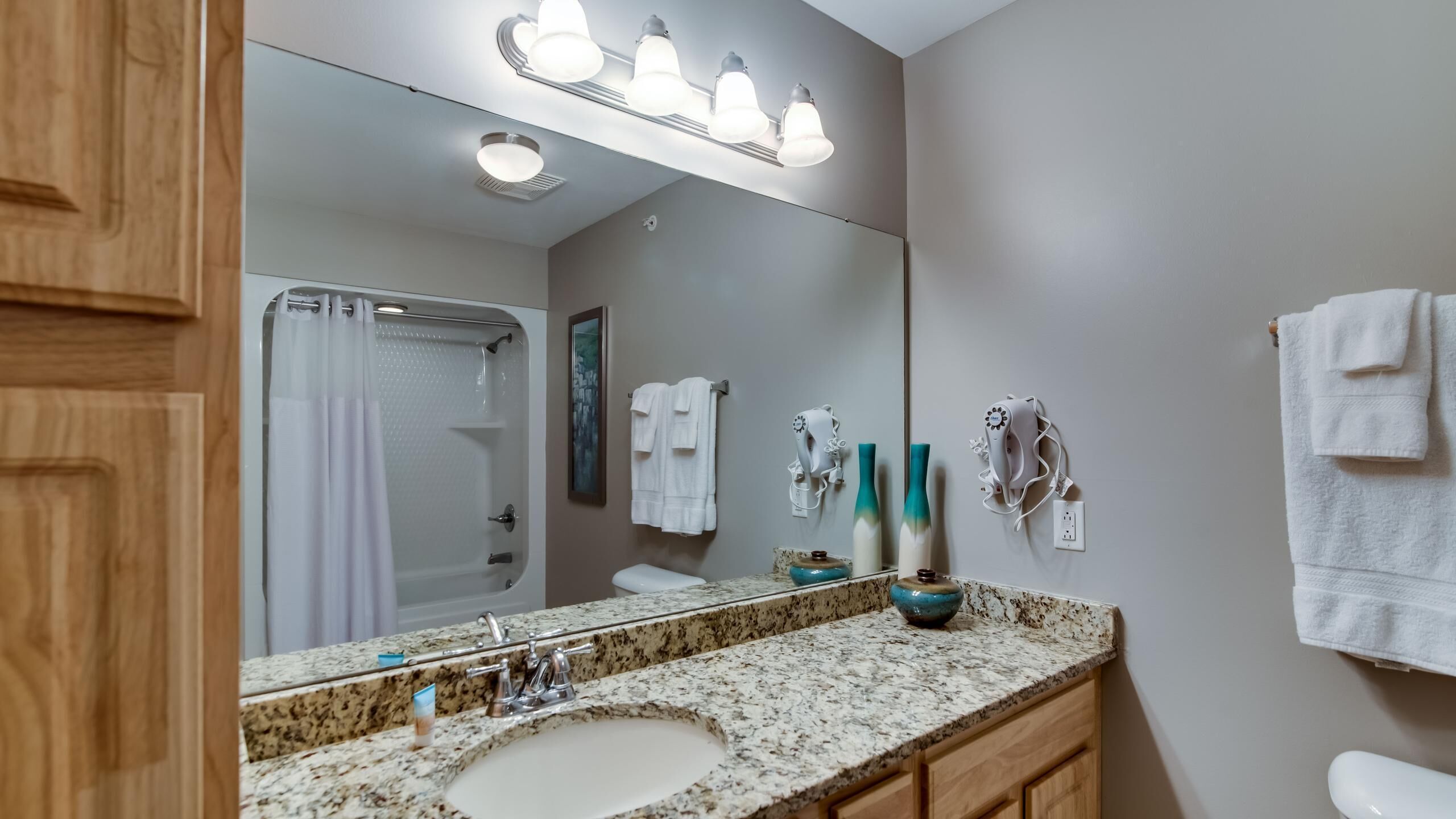 A bathroom with a granite countertop, a sink, a mirror, a shower, and a towel rack.