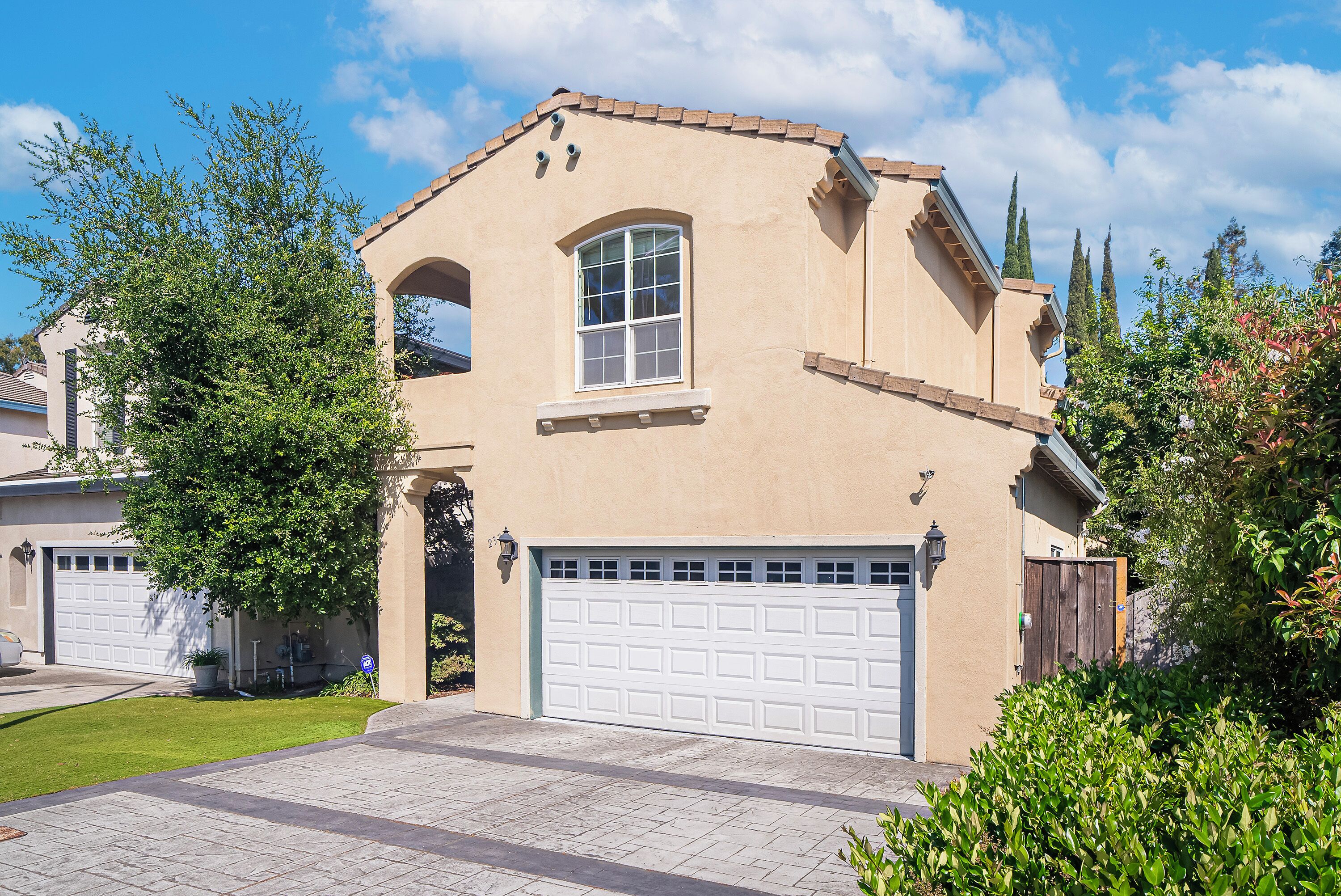 A two-story house with a beige exterior, a white garage door, and a small arched window.