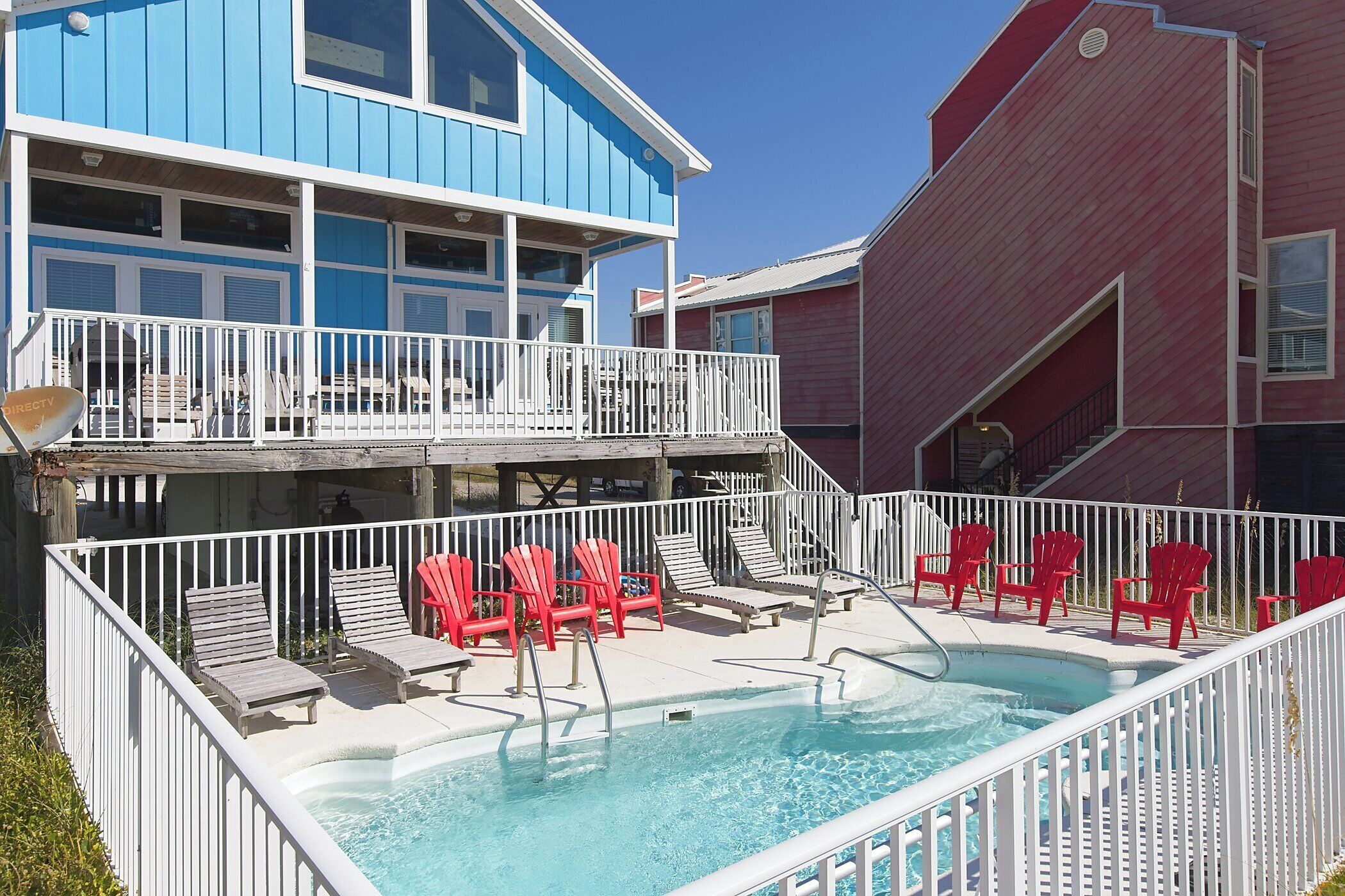 A pool area with red and grey lounge chairs, a white pool fence, and a blue building with a balcony.