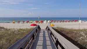 A wooden boardwalk leading to a beach with rows of umbrellas and beach chairs. - Windward Pointe by Southern Vacation Rentals (Orange Beach)