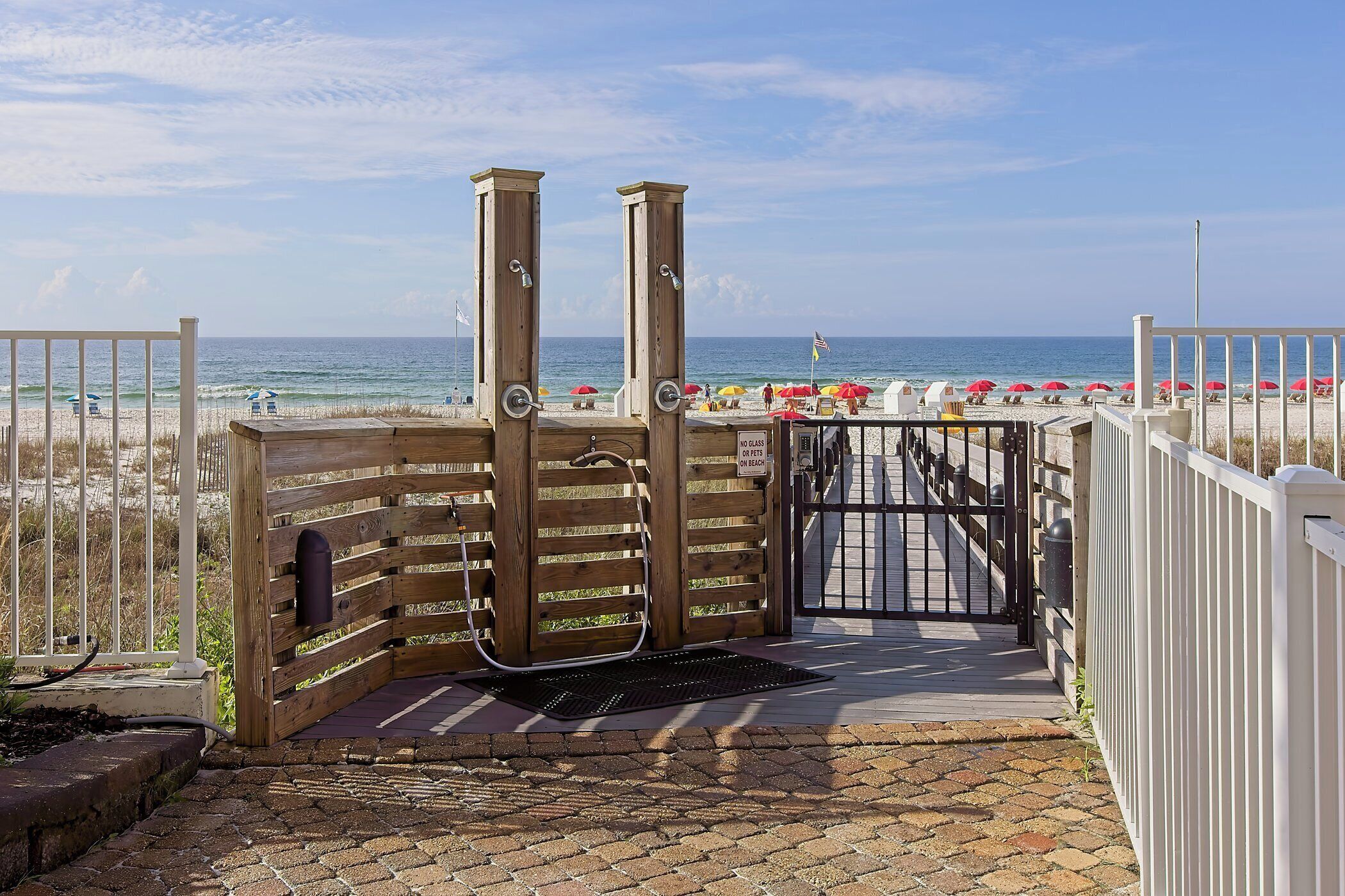 A wooden gate leading to a beach with umbrellas and a clear sky.