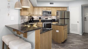 A modern kitchen with wooden cabinets, stainless steel appliances, and a black countertop island with stools. - Windward Pointe by Southern Vacation Rentals (Orange Beach)