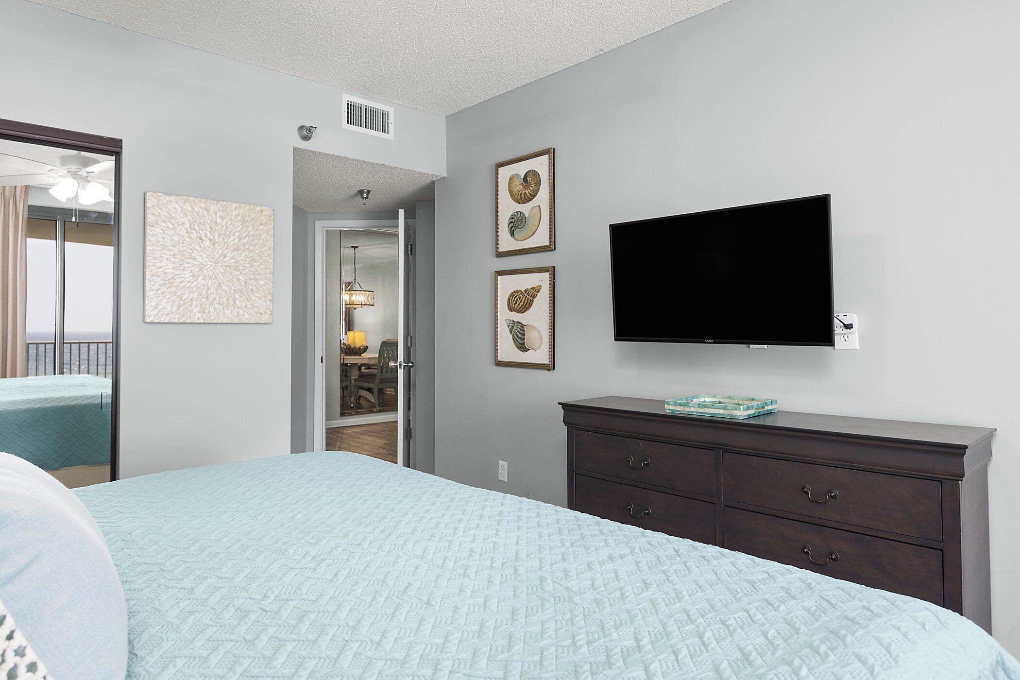 A bedroom with a bed, a dresser, a flat-screen TV, and framed artwork on the wall.