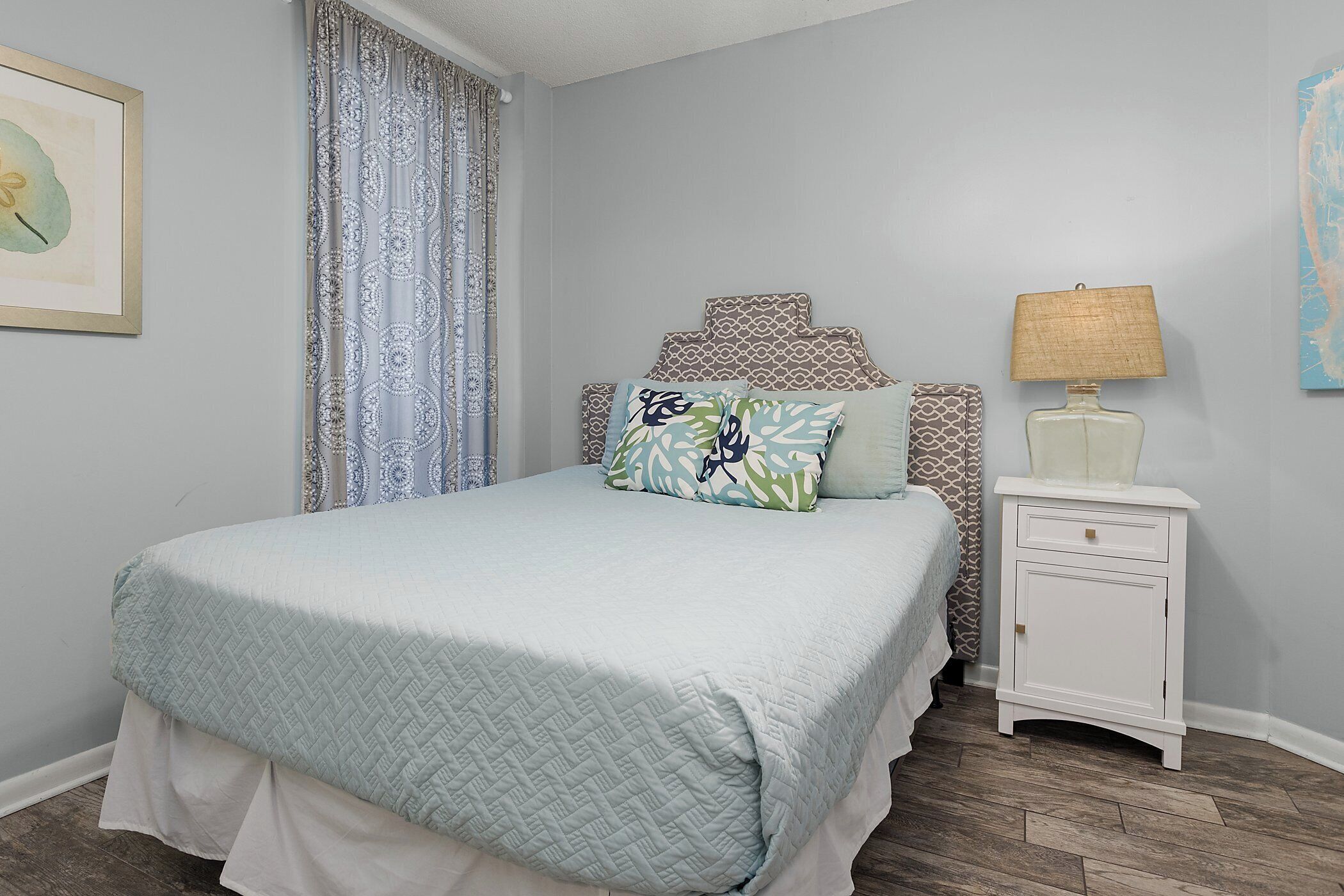 A bedroom with a bed, a nightstand, a lamp, and a curtain.