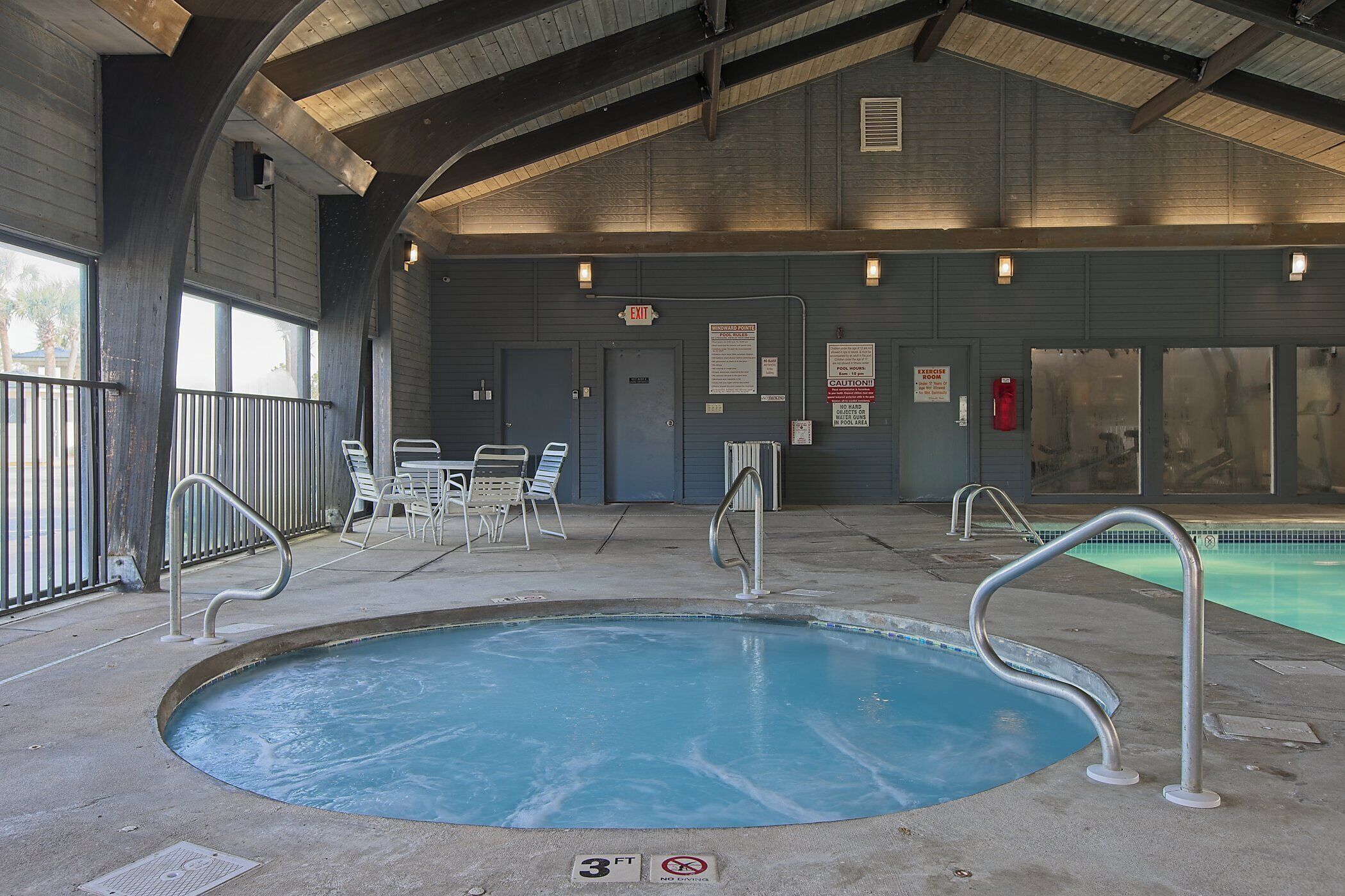 Piscina interior con indicador de profundidad de 0.9 metros, barandales de metal y una zona cubierta con sillas y mesas.