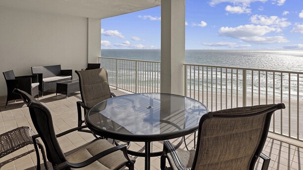 A balcony with a glass table and chairs, overlooking the ocean. - Windward Pointe by Southern Vacation Rentals (Orange Beach)