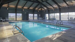 An indoor swimming pool with clear water, surrounded by lounge chairs and tables, under a high ceiling with skylights. - Windward Pointe by Southern Vacation Rentals (Orange Beach)