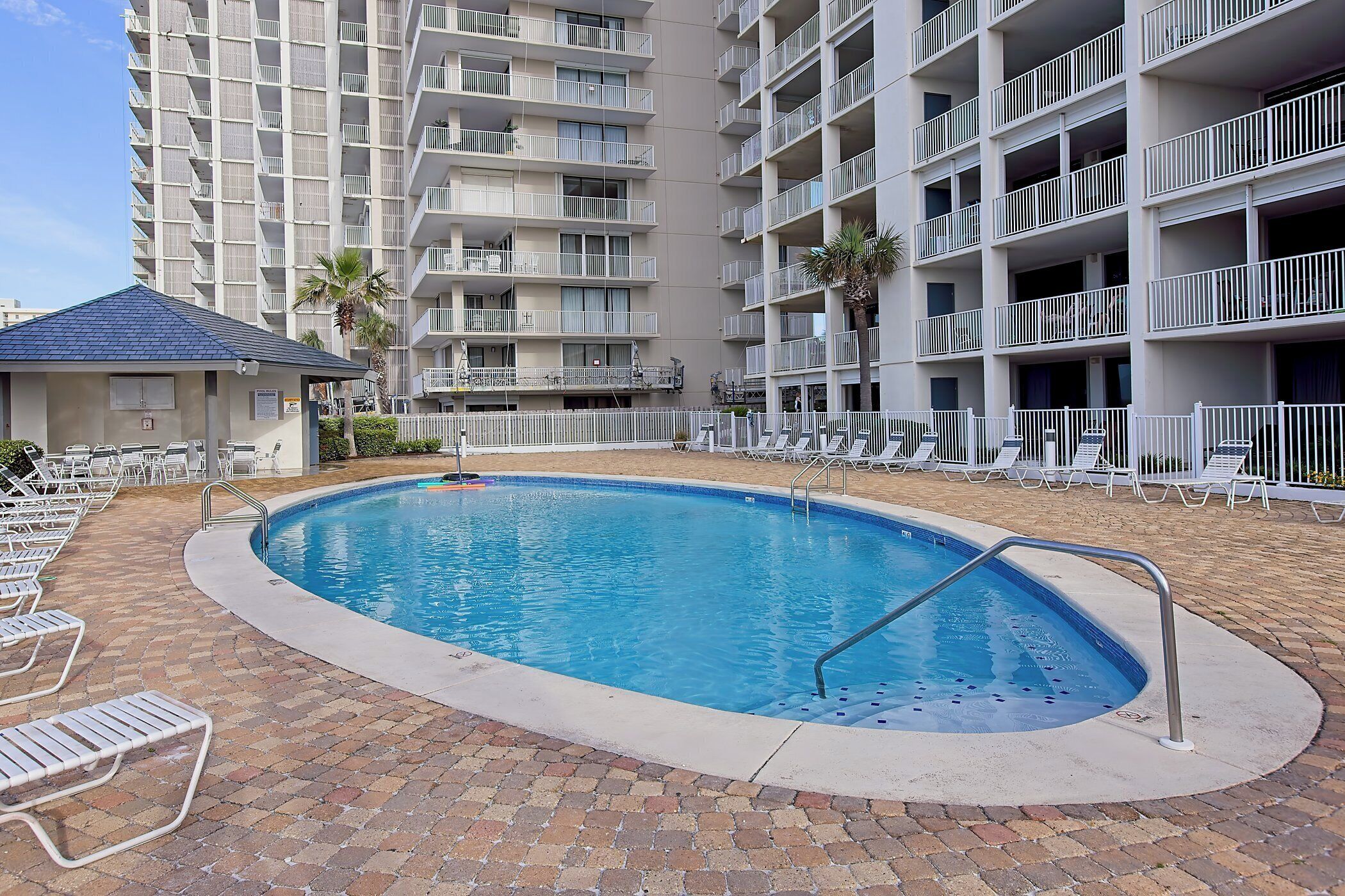 A swimming pool with lounge chairs and a small building, surrounded by multi-story residential buildings.