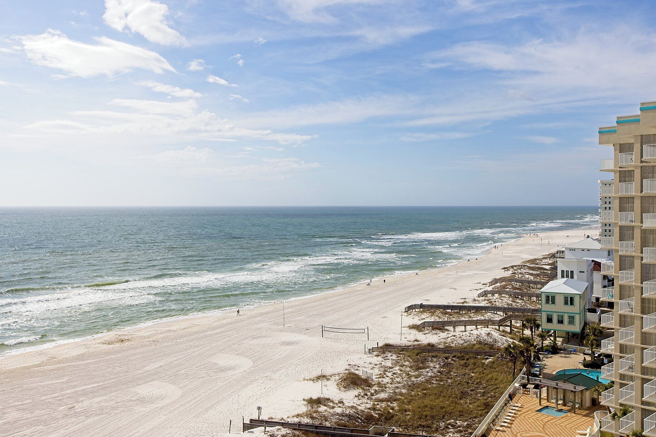 A beach view with a high-rise building, a boardwalk, and a small pool area.