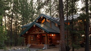 A log cabin with a green roof, a stone foundation, and a wooden porch. - Grand Wildlife Lodge 10ppl (La Pine)