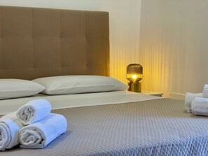 A neatly made bed with pillows, a bedside lamp, and rolled towels. - Apartment on two levels in the historic center in Noto (SR) (Noto)