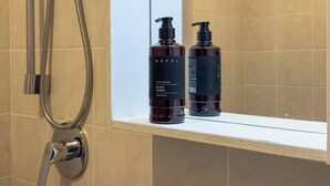 Un baño con ducha, un espejo y dos botellas de NeFEL Black Soap sobre una estantería.