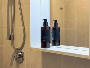 A bathroom with a shower, a mirror, and two bottles of NeFEL Black Soap on a shelf.