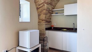 Una cocina compacta con arco de ladrillo, armarios blancos, un refrigerador pequeño y un ventanal.