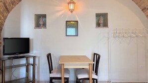 Habitación con televisión sobre una mesa de vidrio, dos sillas, una mesa, lámpara colgante y tendedero.