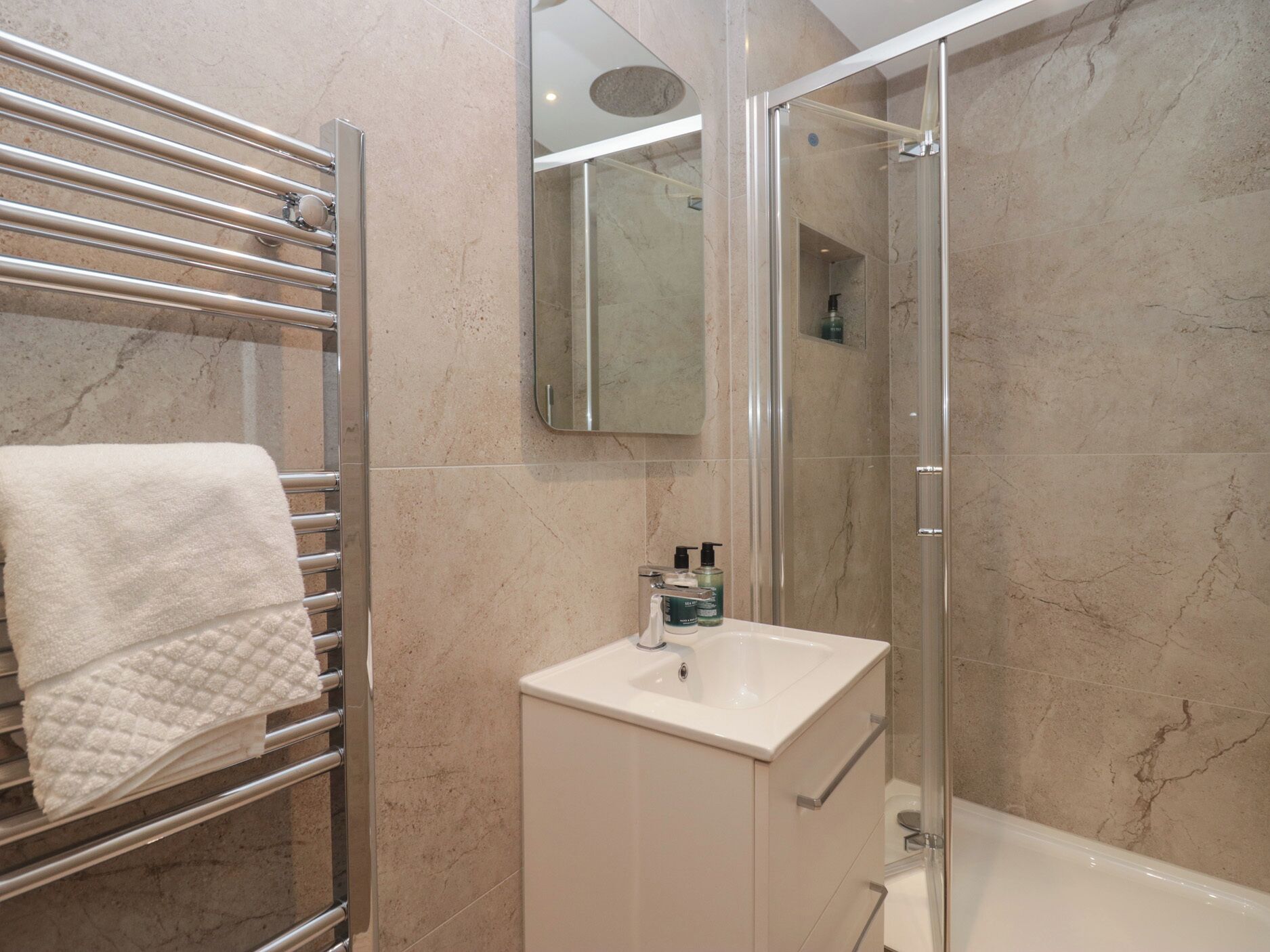 A bathroom with a glass-enclosed shower, a white sink, and a towel rack with a folded towel.
