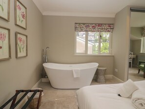 Un bagno con una vasca freestanding, una finestra con tenda floreale e un'opera d'arte con fiori appesa al muro.
