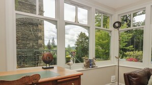 A room with a wooden desk, a leather chair, and large windows with a view of greenery and a stone wall. - The Boundary (Windermere)
