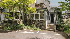 A traditional stone building with a green-tiled roof, a stone staircase leading to a door, and a parking area in front. - The Boundary (Windermere)