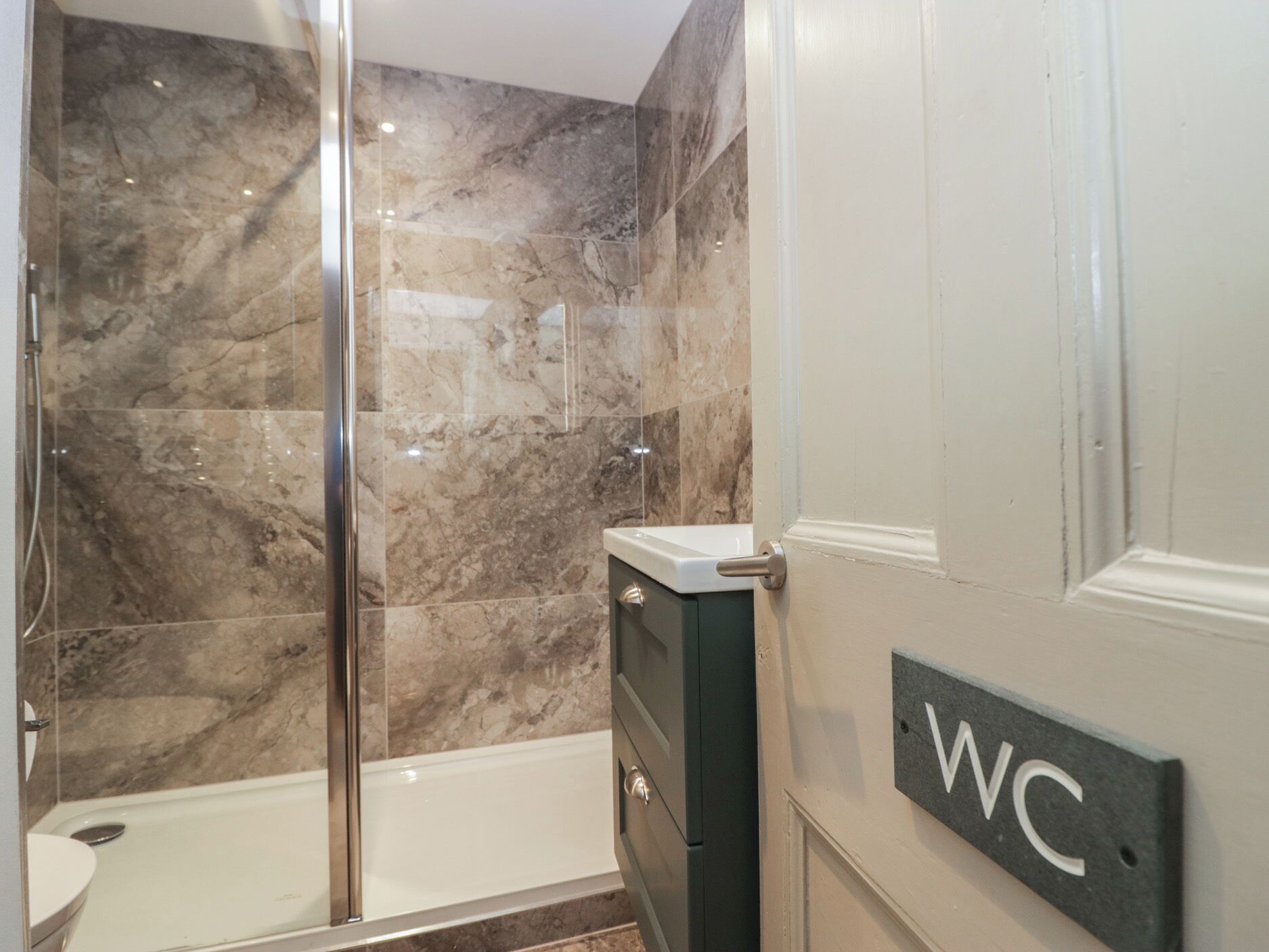 A bathroom with a shower, toilet, and sink, marble walls, and a WC sign.