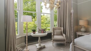 A bedroom with a bed, a chair, a table with a lamp, a potted plant, and a window with curtains. - The Boundary (Windermere)