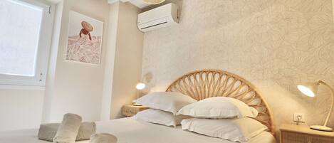 A neatly arranged bedroom with a bed, bedside lamps, and a wall-mounted air conditioner.