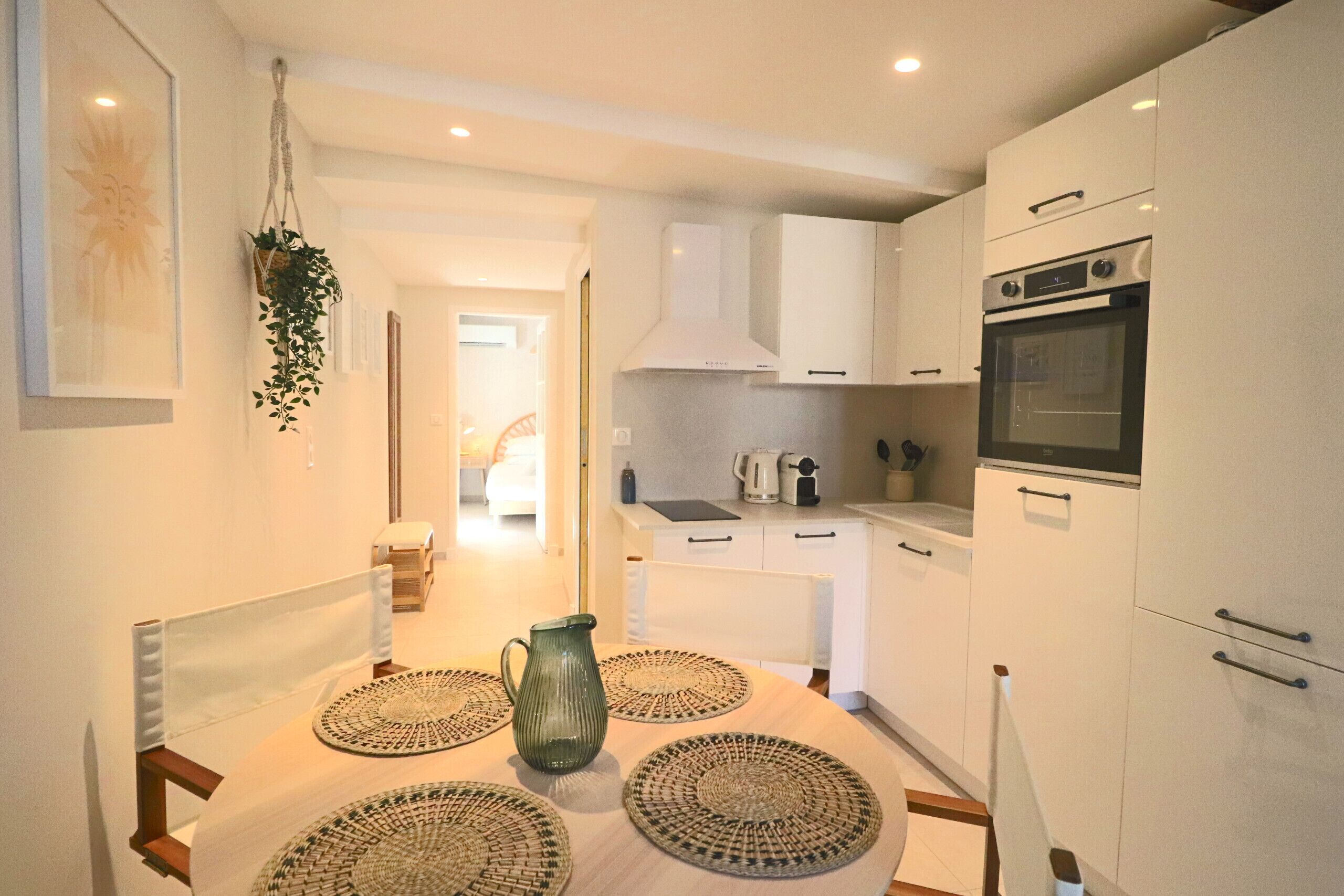 A modern kitchen with white cabinets, a built-in oven, and a dining area with a table set for two.