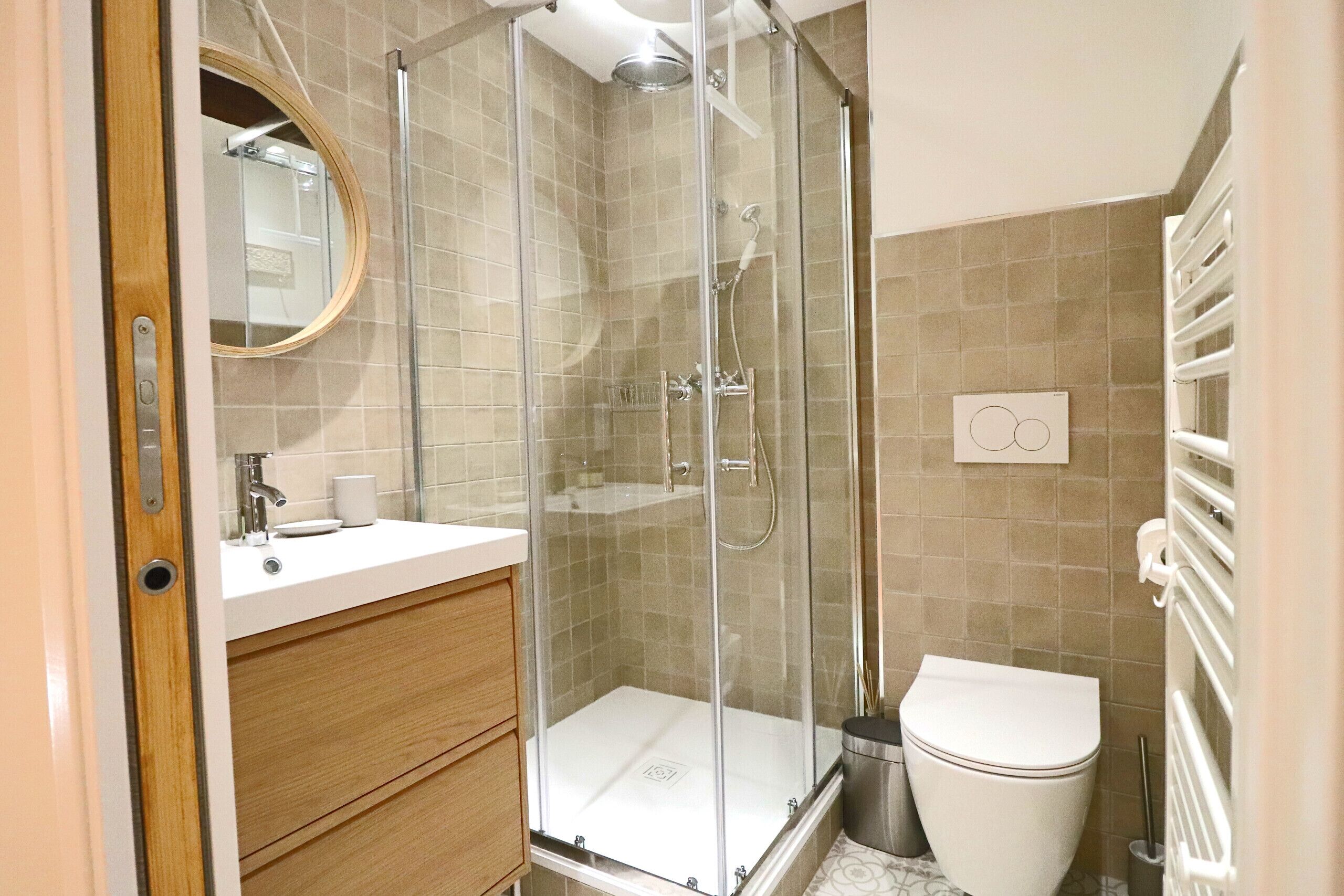 Une salle de bain moderne avec une douche à parois de verre, des toilettes et un lavabo surmonté d’un miroir.