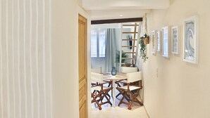 Un couloir avec un coin repas comprenant une table et des chaises blanches, une porte en bois et des œuvres d’art encadrées accrochées au mur.