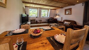 A cozy living room with a wooden ceiling, a television, a fireplace, and a dining area with a table set for two. - La Cachette - Mountain style and spacious 2-Bed apartment central Chamonix (Chamonix-Mont-Blanc)