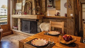 A rustic dining area with a wooden table set for two, a fireplace with a stone surround, and wooden beams on the ceiling. - La Cachette - Mountain style and spacious 2-Bed apartment central Chamonix (Chamonix-Mont-Blanc)